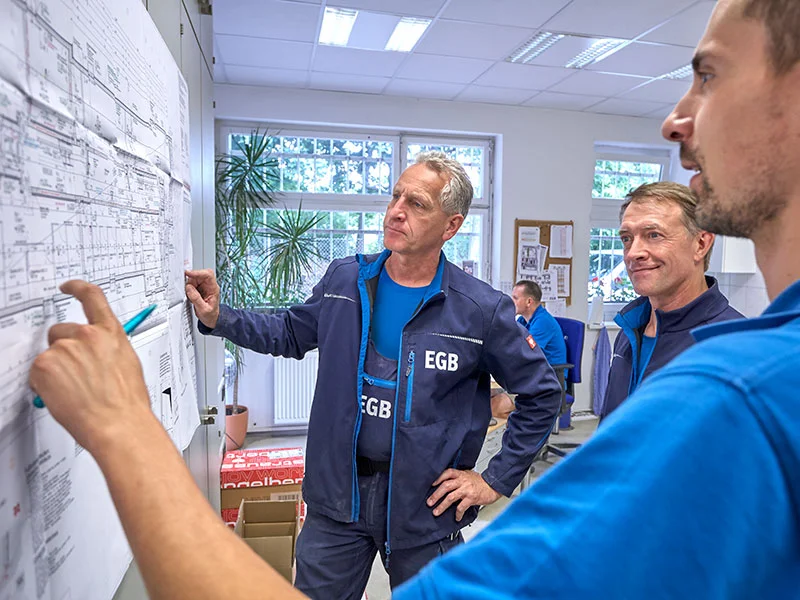 3 Mitarbeiter von EGB planen in einem Büro an einem Plan die genaue Energieversorgung einer Baustelle.