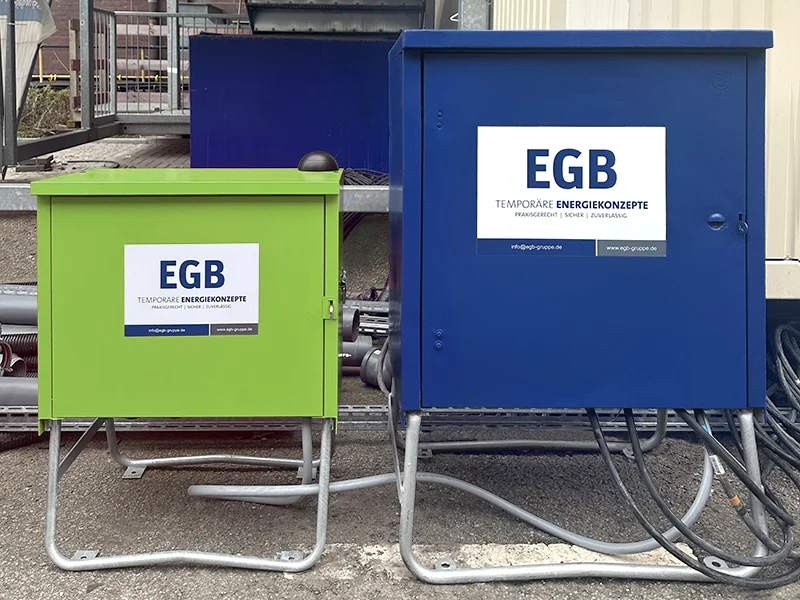 Zwei Stromverteiler von EGB stehen auf einer Baustelle. Der grüne ist etwas kleiner als der blaue